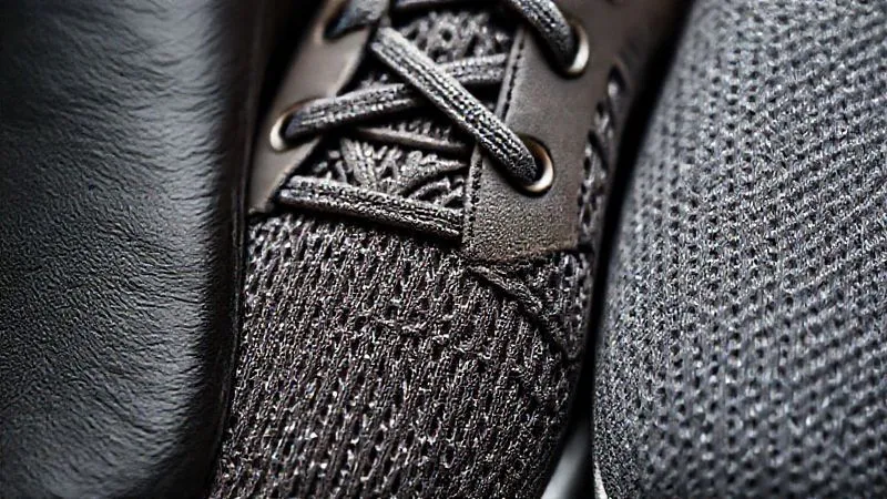 A photorealistic close-up of various high-fashion performance shoe materials: supple leather, intricately woven knit fabric with subtle metallic threads, and a textured, matte-finish synthetic, all arranged aesthetically with dramatic studio lighting, sharp focus on the textures, 8K, cinematic lighting, depth of field.