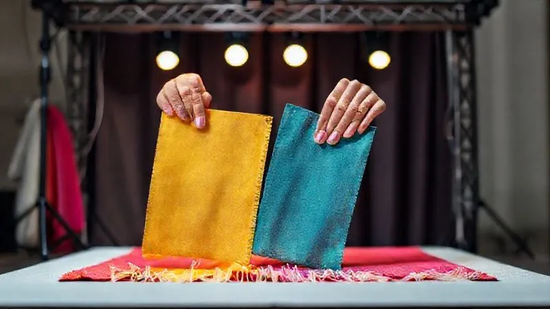 A photorealistic image of a costume designer meticulously placing fabric swatches on a miniature stage set under a scaled stage lighting rig. One swatch clearly shows fading, while another retains its vibrancy. Professional photography, 8K, cinematic lighting, sharp focus on the swatches and designer's hands, depth of field blurring the background, shot on a high-end DSLR.