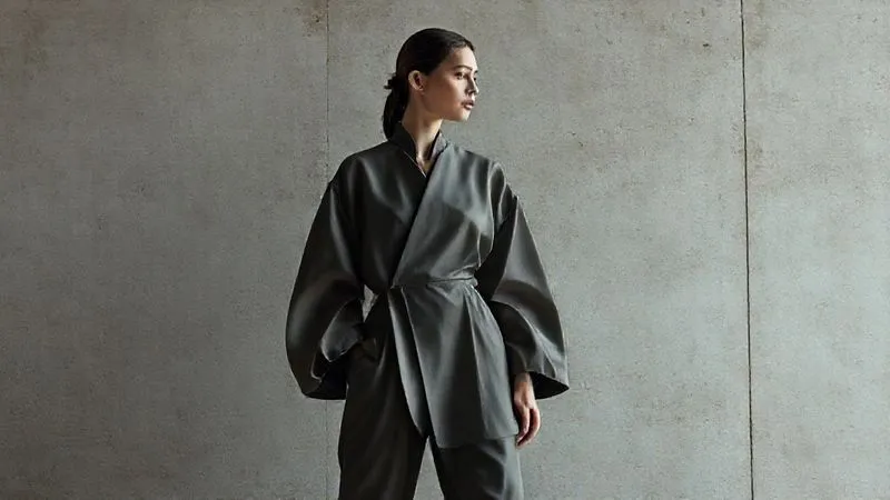 photorealistic, professional photography, 8K, cinematic lighting, sharp focus, depth of field, shot on a high-end DSLR, a minimalist fashion shot featuring a model in a single, striking architectural garment with exaggerated sleeves, captured against a clean, textured concrete wall, emphasizing the interplay of light and shadow on the fabric's unique form and silhouette, with a very subtle, almost monochromatic color palette.