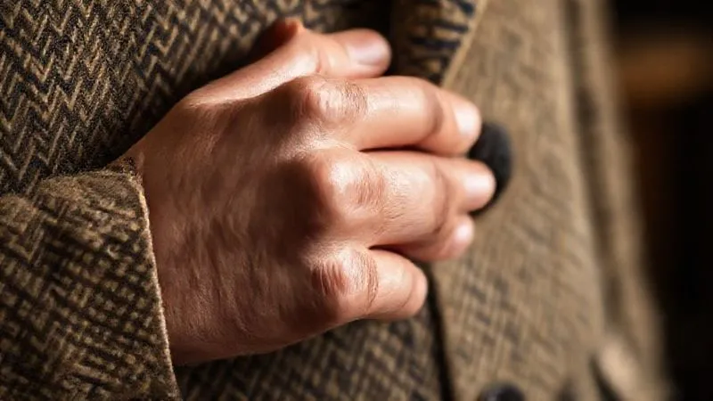 A photorealistic, close-up professional photography shot of a discerning hand gently feeling the luxurious texture of a vintage wool tweed jacket, examining the intricate stitching and quality of the fabric. The background is softly blurred, focusing on the tactile interaction, cinematic lighting, sharp focus, depth of field, 8K hyper-detailed, shot on a high-end DSLR.