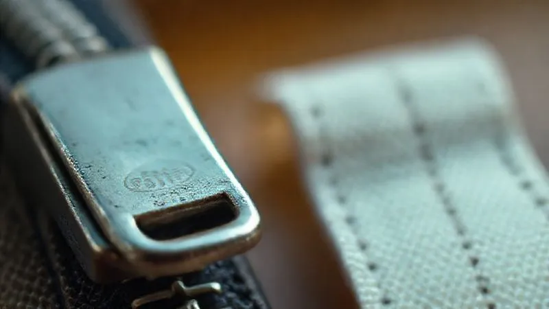 Photorealistic, professional photography, 8K, cinematic lighting, sharp focus, depth of field, shot on a high-end DSLR, a close-up comparison of a vintage metal zipper pull with a clear brand mark (e.g., 'Talon') next to a generic, flimsy modern plastic zipper pull. The image highlights the difference in material, weight, and craftsmanship, with a subtle focus on the texture of the zipper tape.