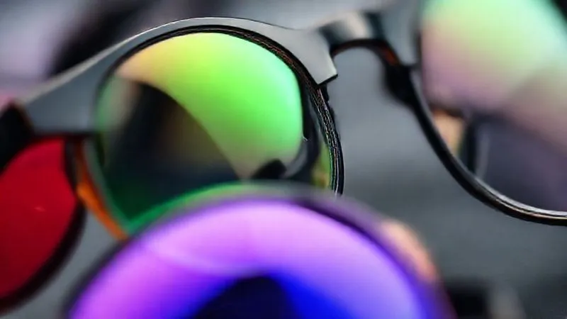A close-up, photorealistic shot of various eyeglasses lenses showcasing different coatings and materials. One lens clearly shows an anti-reflective green hue, another a blue light filter, and a third appears ultra-thin high-index. Cinematic studio lighting, sharp focus on the lens surfaces, depth of field blurring the background, 8K, professional photography, shot on a high-end DSLR.