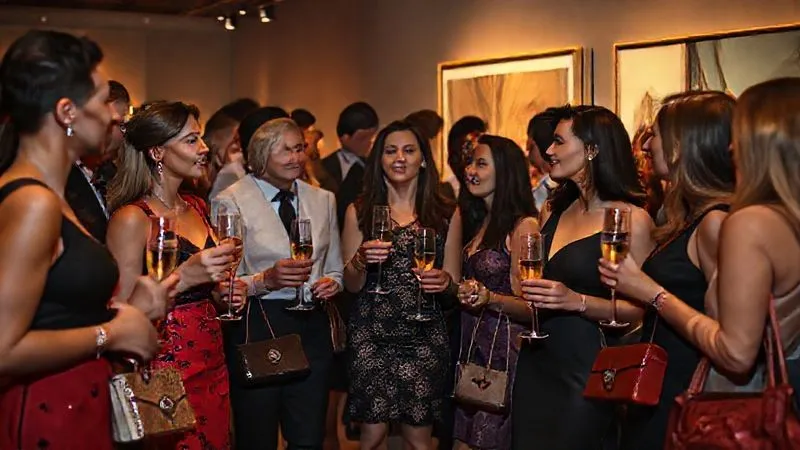 A diverse group of elegantly dressed individuals, holding unique luxury accessories, engaging in lively conversation at an exclusive, dimly lit art gallery event, champagne flutes in hand. The atmosphere is sophisticated and intimate, with subtle brand presence. Photorealistic, professional photography, 8K, cinematic lighting, sharp focus on the interactions, depth of field, shot on a high-end DSLR.