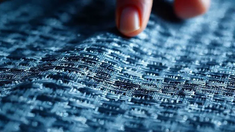 A photorealistic, professional photography, 8K, cinematic lighting, sharp focus, depth of field, shot on a high-end DSLR of a close-up, tactile shot of an innovative textile with a unique woven pattern and subtle reflective threads, showcasing the intricate texture and advanced material properties. The lighting should highlight the depth and complexity of the fabric, possibly with a hand gently touching it.