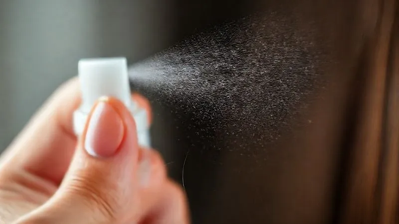 A close-up, photorealistic image of a fine mist of heat protectant being sprayed onto a section of fine, damp hair held between fingers. The spray creates a delicate, even coating. Cinematic lighting, sharp focus on the hair and mist, depth of field blurring the background, 8K hyper-detailed, professional photography, shot on a high-end DSLR.