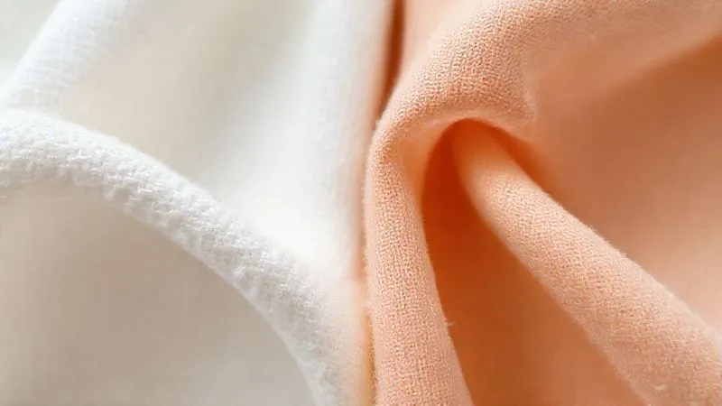 A photorealistic close-up of two distinct fabric swatches side-by-side: one a visibly soft, brushed cotton, and the other a performance synthetic fabric with a similarly soft, 'peached' finish. Both show subtle textures and inviting colors, under soft, diffused studio lighting, 8K, cinematic, sharp focus, depth of field.