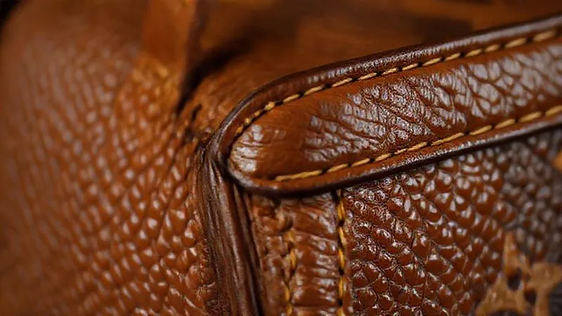 A close-up, photorealistic image showcasing the texture of authentic, aged Vachetta leather on a vintage Louis Vuitton bag handle next to a perfectly aligned seam with precise stitching. Cinematic lighting, sharp focus on the material's grain and patina, 8K, professional photography, depth of field.