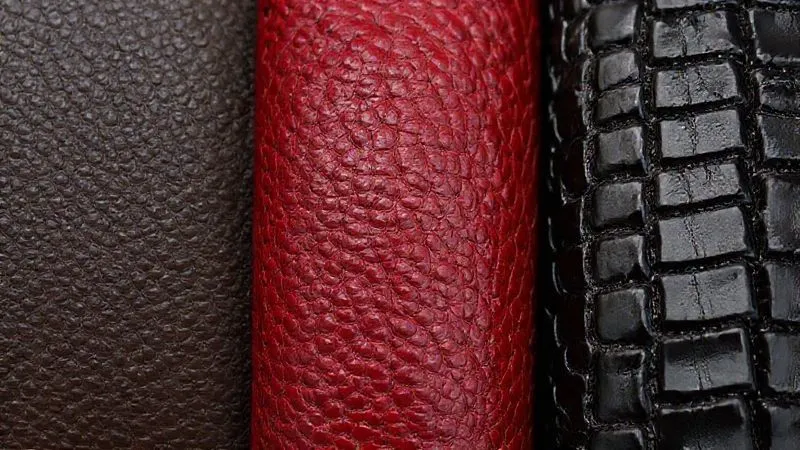 A macro, photorealistic close-up of three distinct leather textures side-by-side: the fine, smooth grain of dark brown calfskin, the characteristic ripple of burgundy shell cordovan, and the unique scale pattern of a black alligator leather, each bathed in soft, natural light, highlighting their individual textures and finishes. Sharp focus, depth of field, 8K hyper-detailed, professional photography, shot on a high-end DSLR.