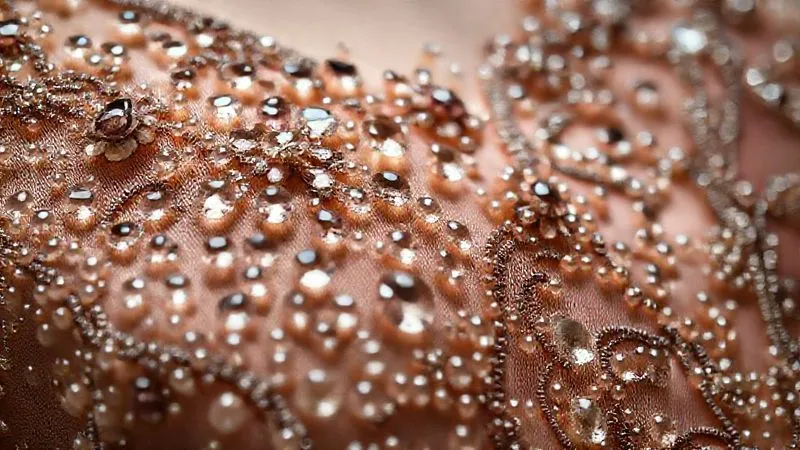 A close-up, photorealistic shot of intricate, hand-sewn glass beadwork on a vintage silk flapper dress, with some beads showing a gentle patina of age, professional photography, 8K, cinematic lighting, sharp focus, depth of field, shot on a high-end DSLR.