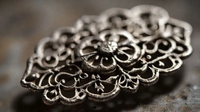 A macro shot of a delicate, tarnished antique silver filigree brooch with tiny cracks visible in the metalwork, under soft, focused lighting, emphasizing its age and fragility. Photorealistic, professional photography, 8K, cinematic lighting, sharp focus, depth of field, shot on a high-end DSLR.