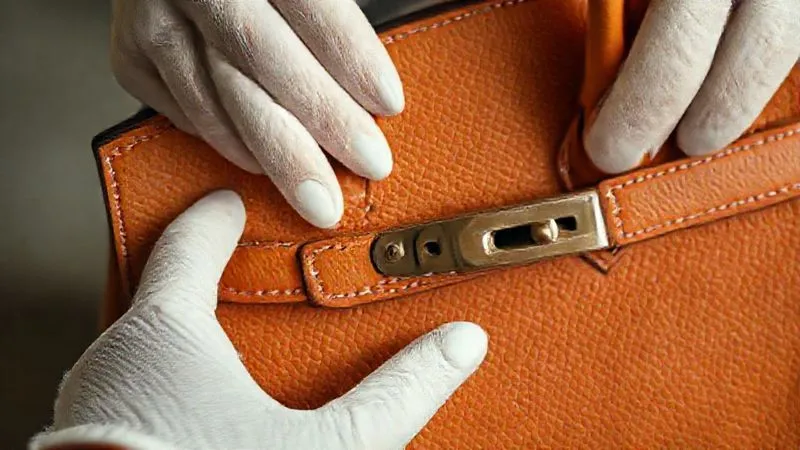 A close-up, photorealistic shot of the intricate stitching and hardware on a vintage Hermes Birkin bag, held by elegant, gloved hands. Soft, diffused cinematic lighting, sharp focus on details, 8K, professional photography, conveying luxury and craftsmanship.