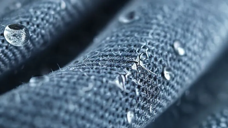A close-up, photorealistic, professional photography, 8K, cinematic lighting, sharp focus, depth of field, shot on a high-end DSLR, showing a microscopic view of a silver-coated thread within a textile, exhibiting tiny cracks and delamination along its surface, with blurred water droplets in the background, symbolizing mechanical wear from washing.